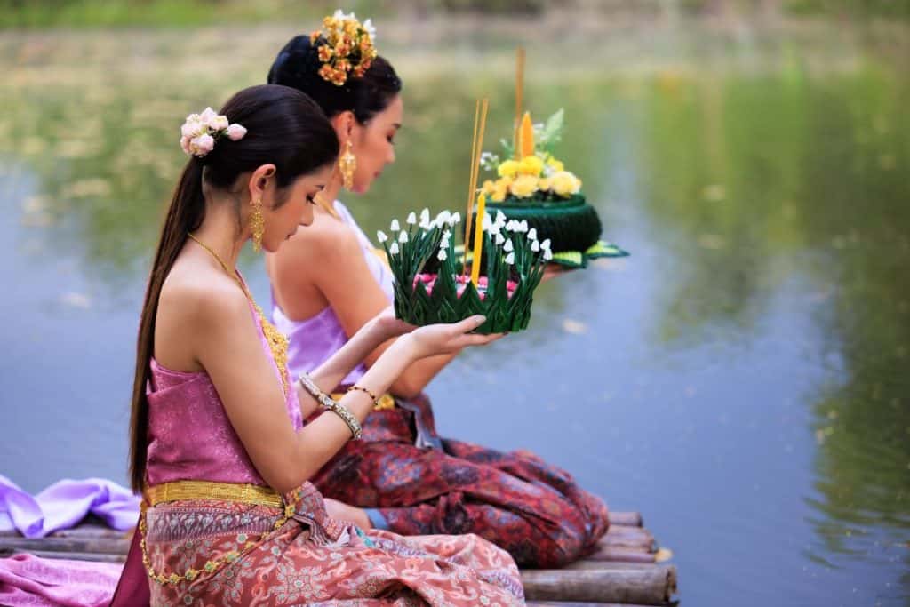 Two Thai women prepare to float krathongs on the water during the Thailand lantern festival.